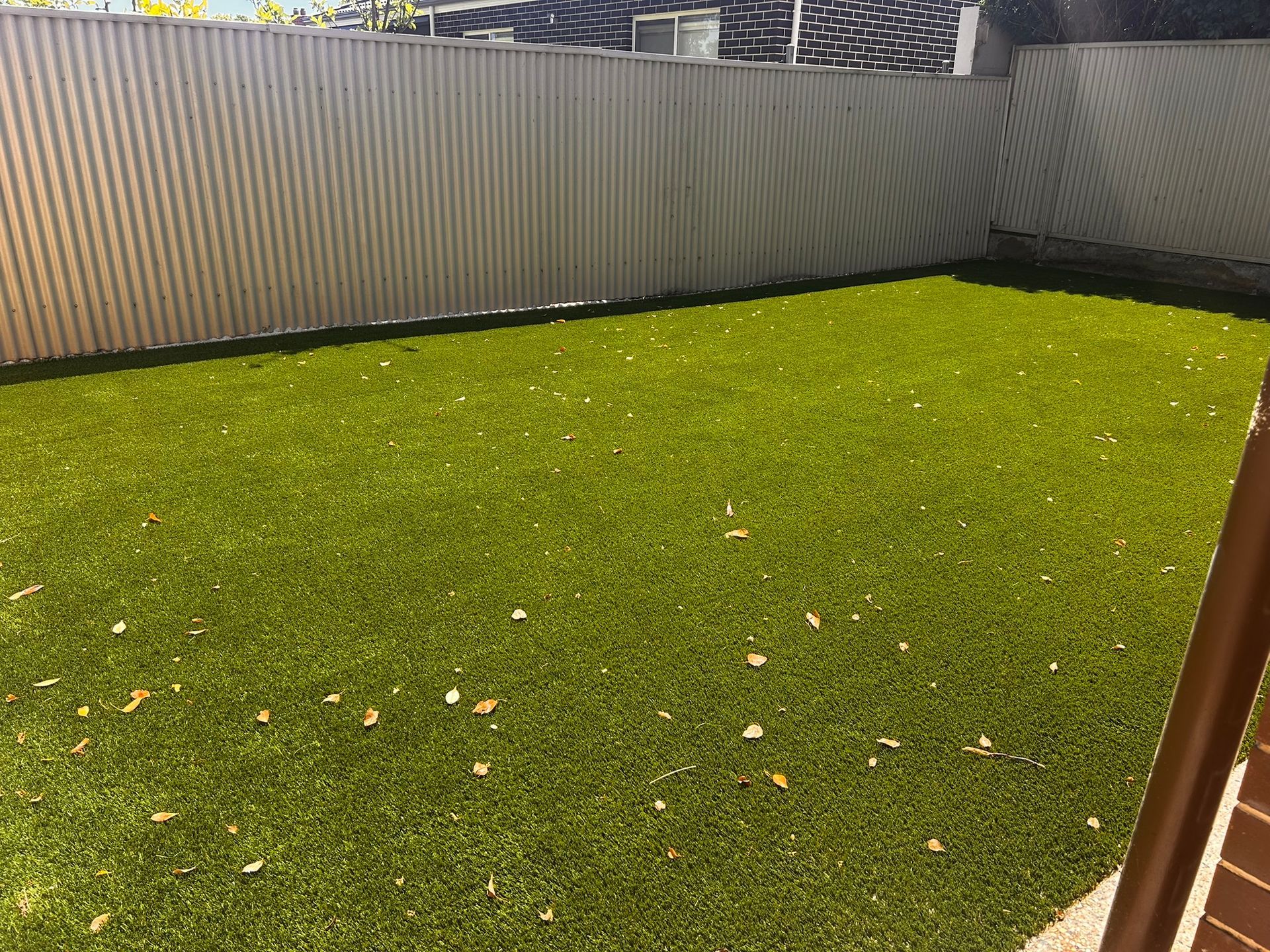 Small backyard with bright green lawn, corrugated metal fence, and a wooden post in the foreground.