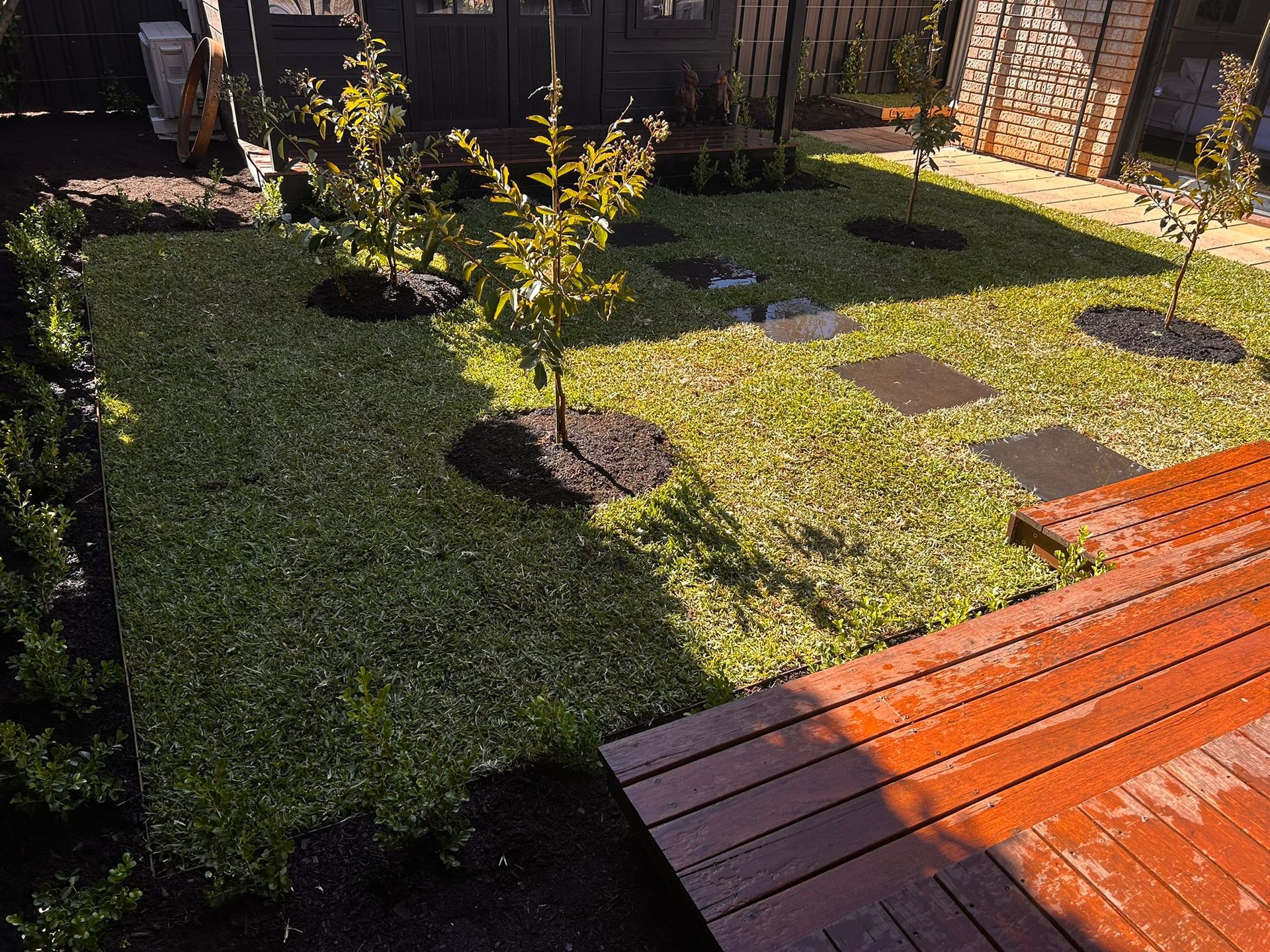 Rainy backyard with wet grass, puddles, bare trees, and a fence beside a white van