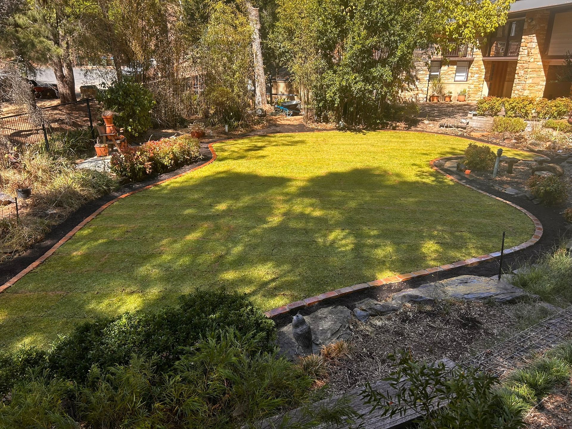 Sunlit landscaped garden with a curved lawn, flower beds, and stone edging