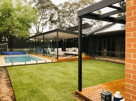 Backyard patio with pool, lawn, and covered outdoor seating beside a brick house Backyard patio with pool, lawn, and covered outdoor seating beside a brick house
