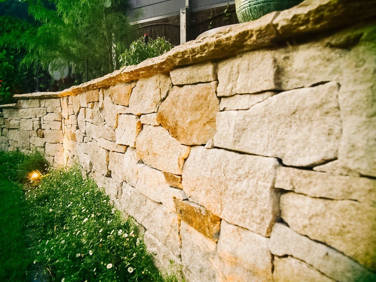 Stone retaining wall beside a grassy slope with small white flowers and a building above Stone retaining wall beside a grassy slope with small white flowers and a building above