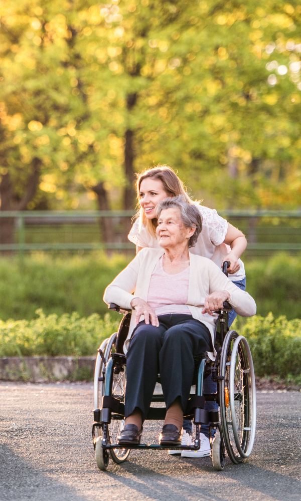 A person pushing an older individual in a wheelchair along an outdoor path during golden hour.