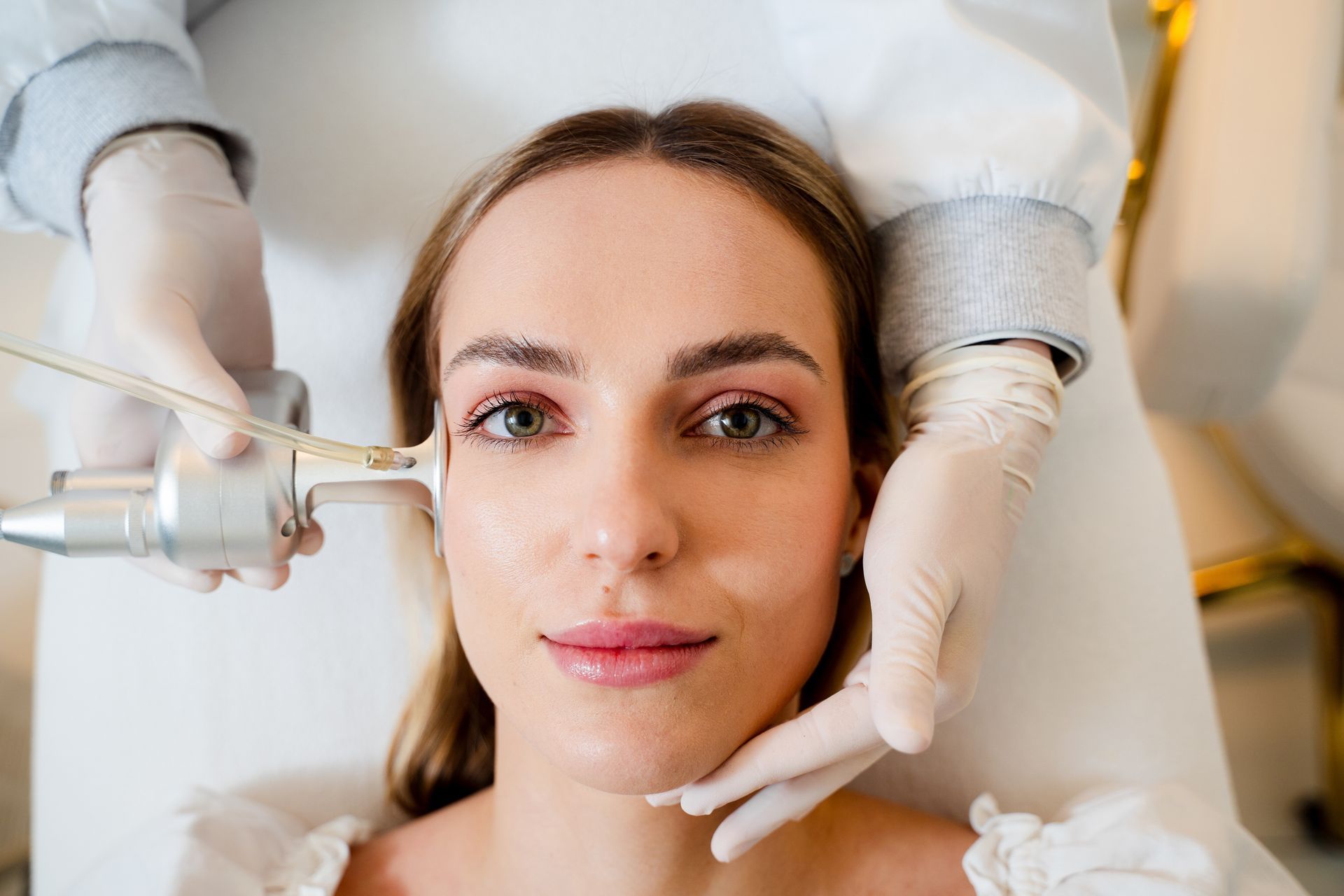 A professional uses a facial treatment tool on a person's cheek in a bright, clinical setting.