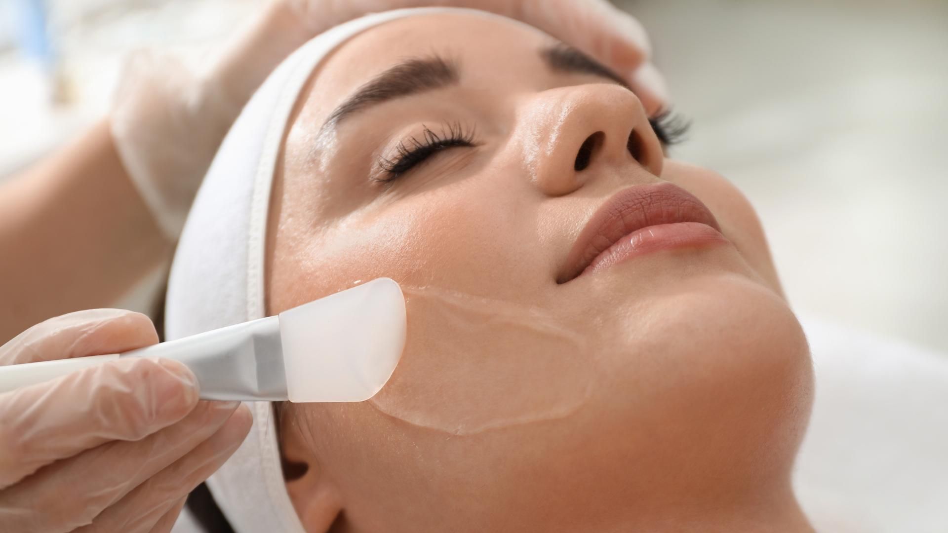 Cosmetician applying a facial treatment with a white spatula to a reclining client