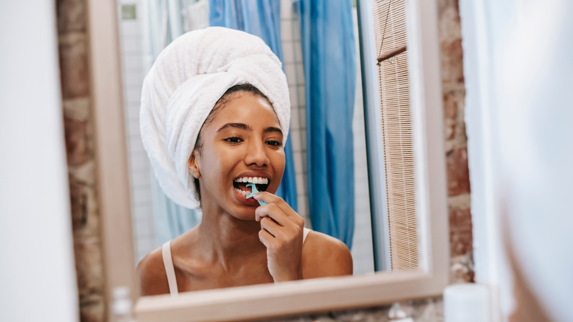 Woman standing in mirror flossing with floss pick.