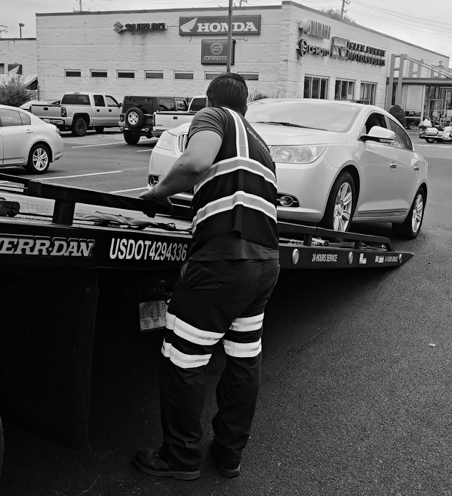 A black and white photo of a tow truck carrying a car