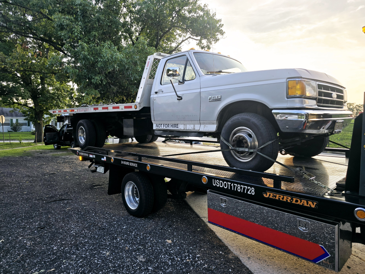 A white truck is sitting on top of a tow truck.