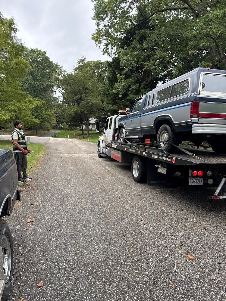 A man is standing next to a tow truck with a car on the back.