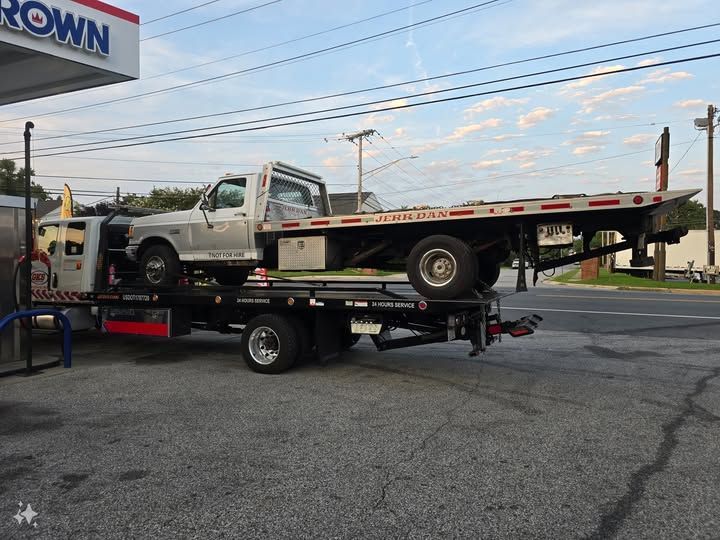 A tow truck with a car on it is parked in front of a crown gas station
