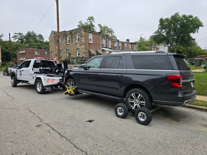 A black suv is being towed by a white tow truck.