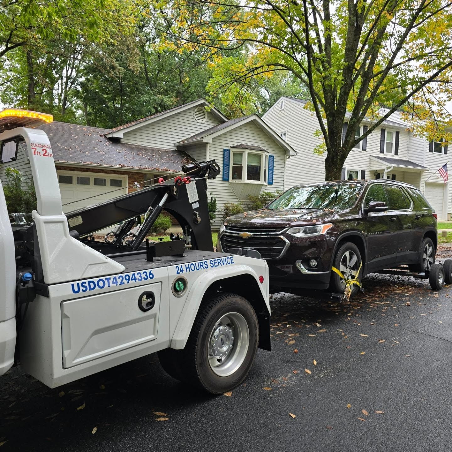 A tow truck is towing a car in front of a house.