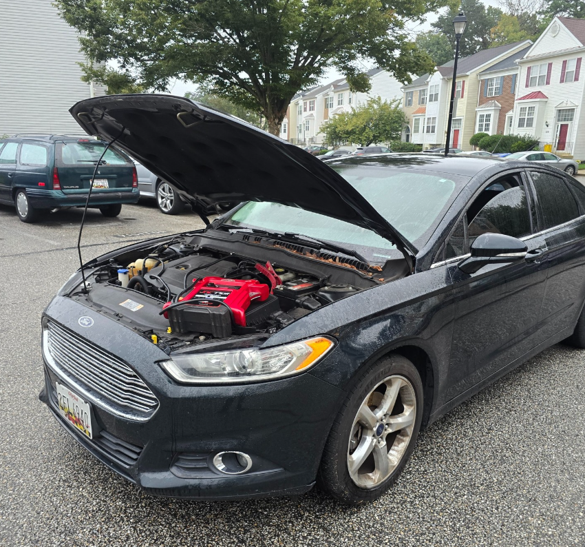 A black car with the hood up is parked in a parking lot
