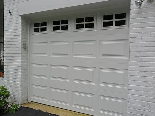 A white garage door is on a white brick building.