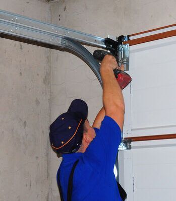 A man is working on a garage door with a drill.