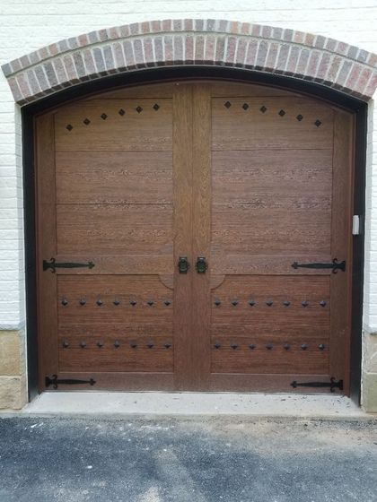 A wooden garage door with a brick arch on a white brick building.