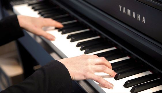 Hands playing keys on a black Yamaha piano.