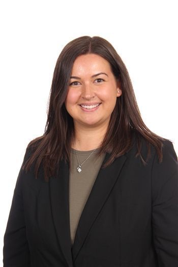 Lächelnde Frau in einem schwarzen Blazer über einem olivgrünen Top vor weißem Hintergrund