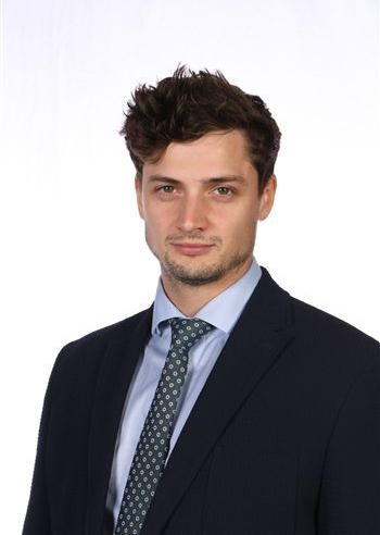 Studioaufnahme eines Mannes in einem dunklen Anzug und einer gemusterten Krawatte vor weißem Hintergrund