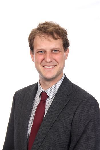 Lächelnde Person mit Brille und Blazer vor einem schlichten weißen Hintergrund