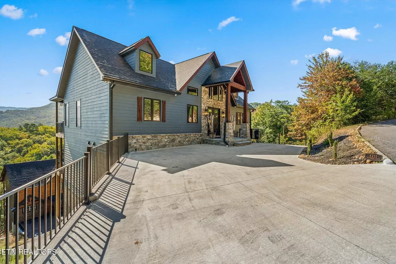 Modern house with stone siding and large driveway overlooking a wooded valley