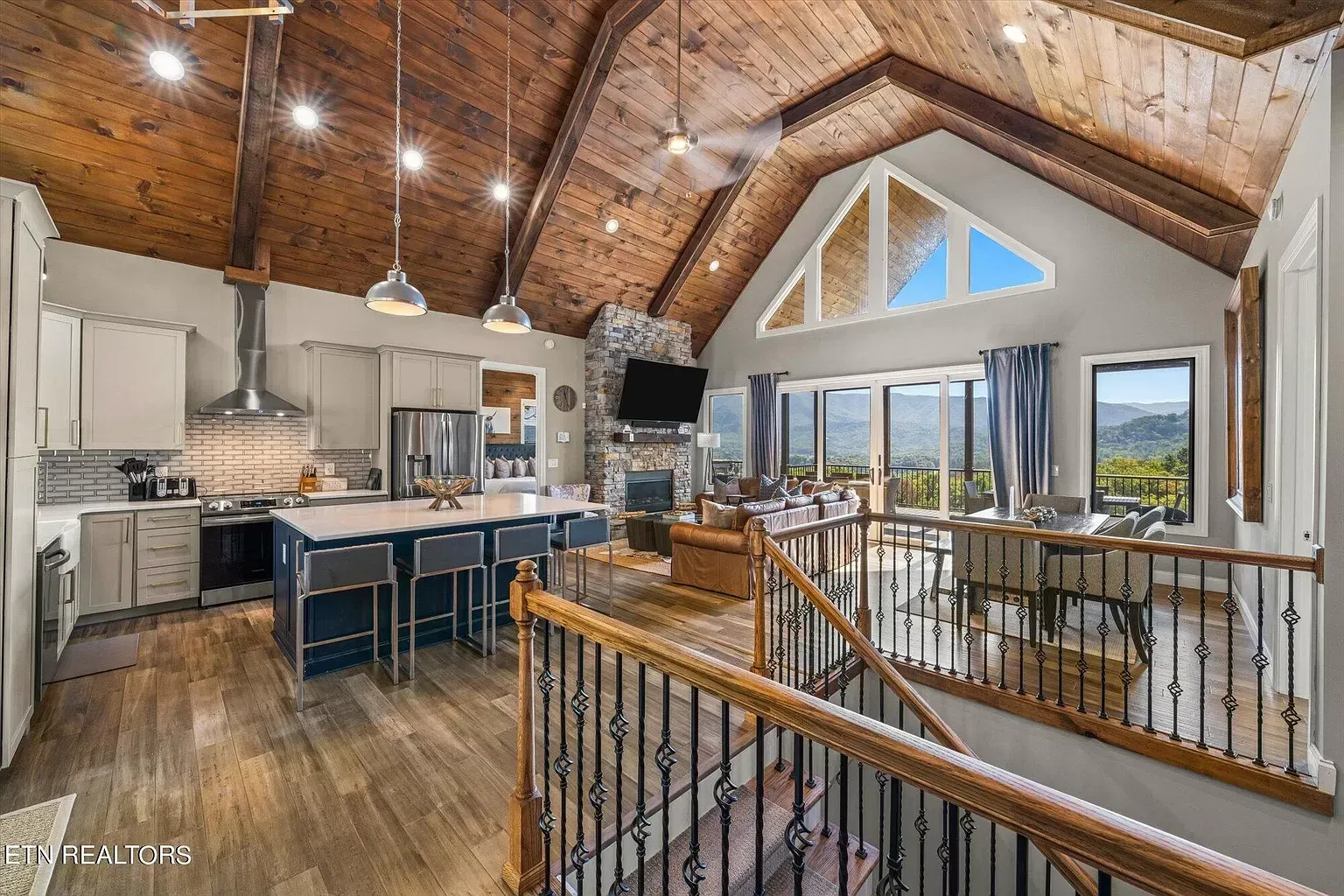 A kitchen , living room , and stairs in a house with a vaulted ceiling.