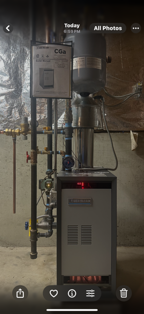 Wall-mounted mechanical equipment and pipes in a dim utility room, with a small control box and indicator light.