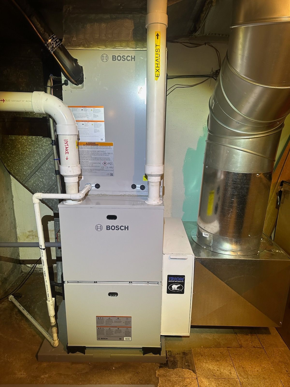 Bosch furnace with white vent pipes and metal ductwork in a utility room