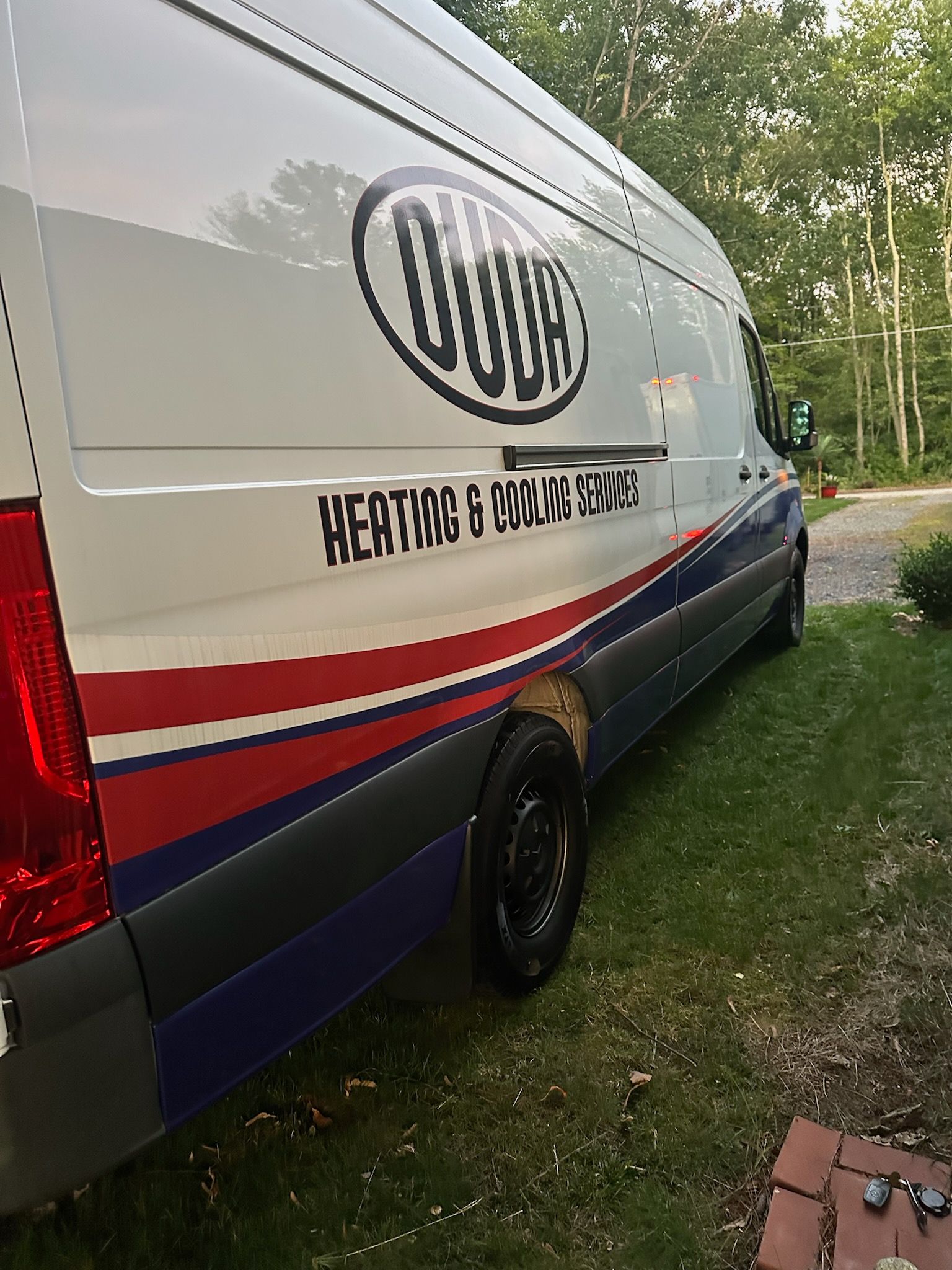 White and blue van with red stripes parked on grass near a path
