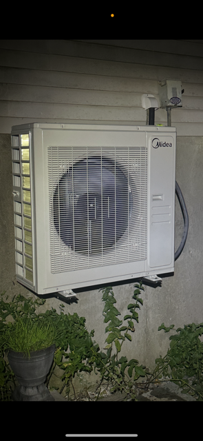 Outdoor wall-mounted air conditioner unit beside a house wall at night
