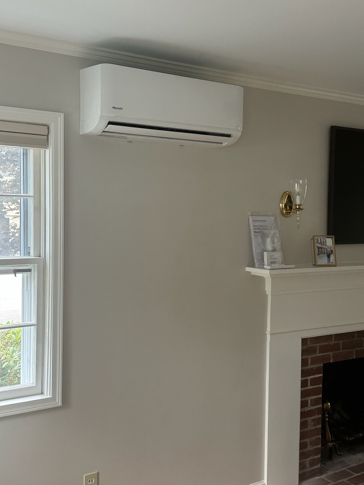Living room wall with a white air conditioner above a window and fireplace mantel