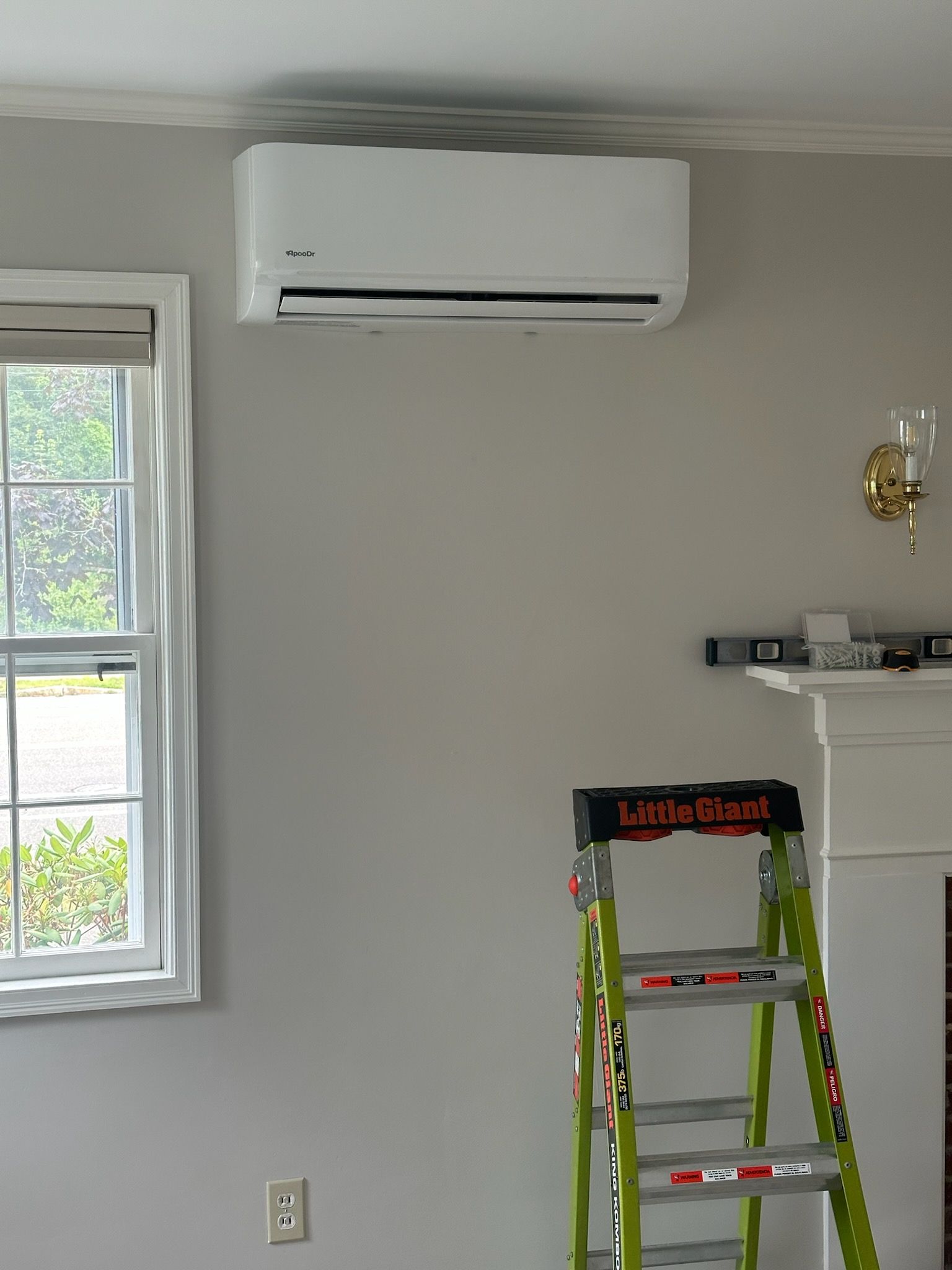 Bright room with wall-mounted air conditioner, window, and ladder near a small shelf.
