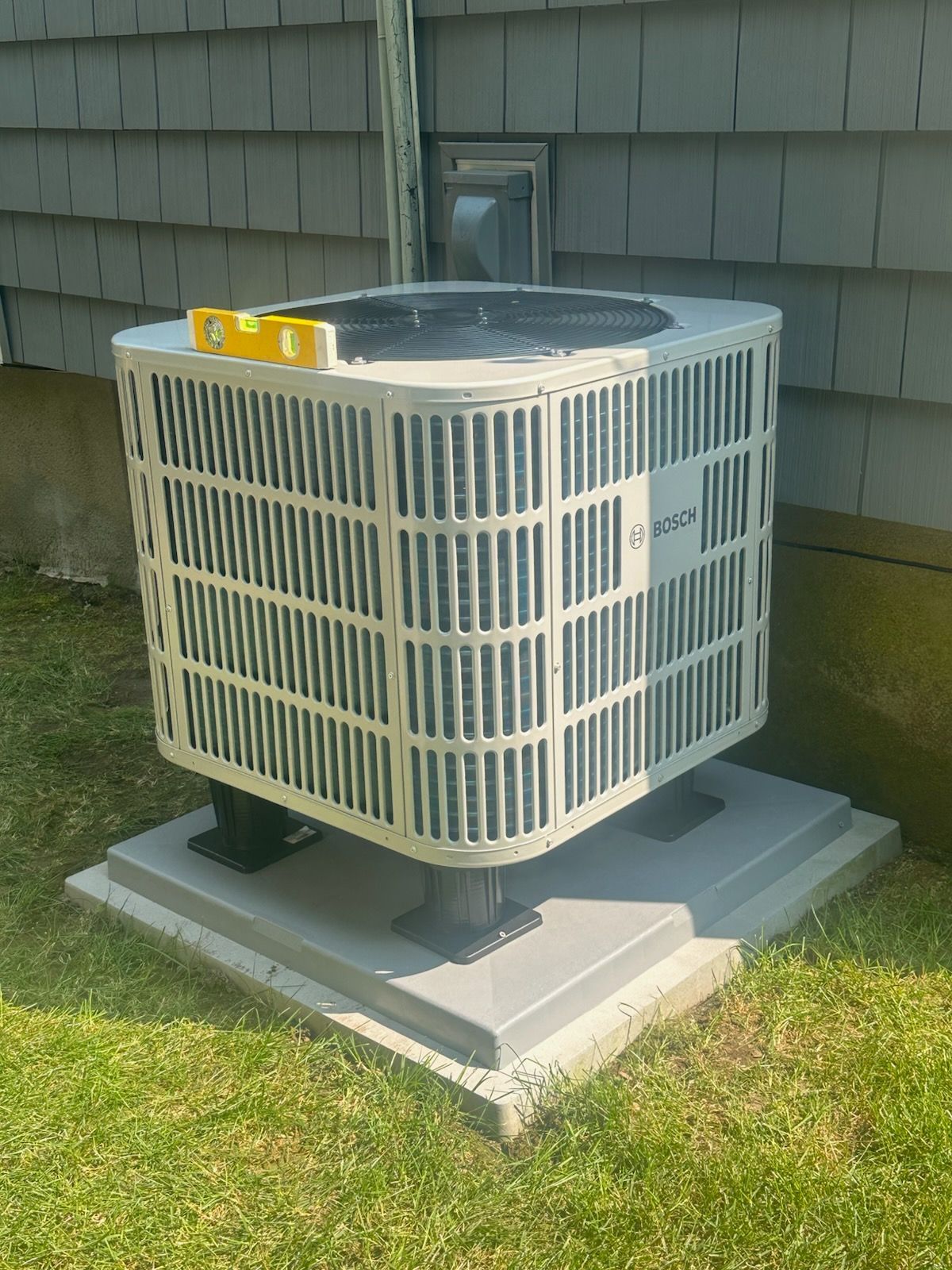 Outdoor air conditioner unit on a concrete pad beside a house wall and grass.