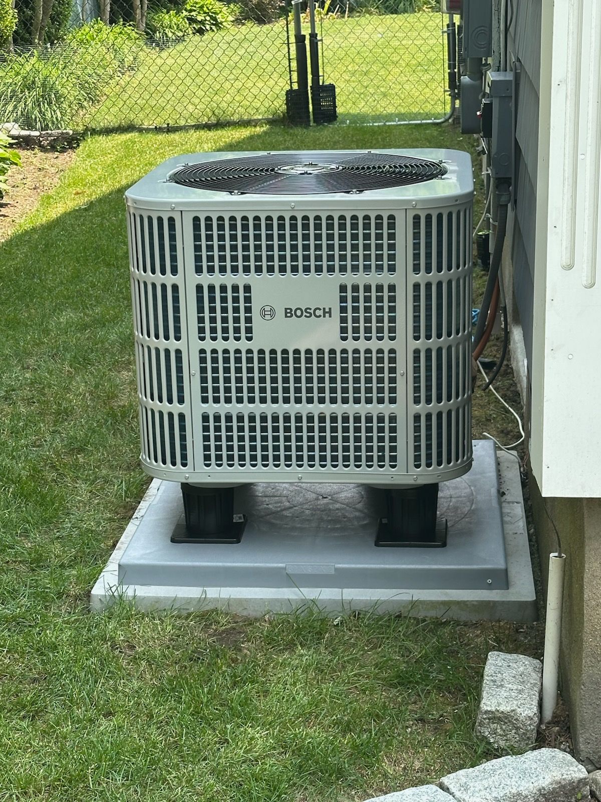 Outdoor Bosch air conditioner unit on a concrete pad beside a house and grassy yard