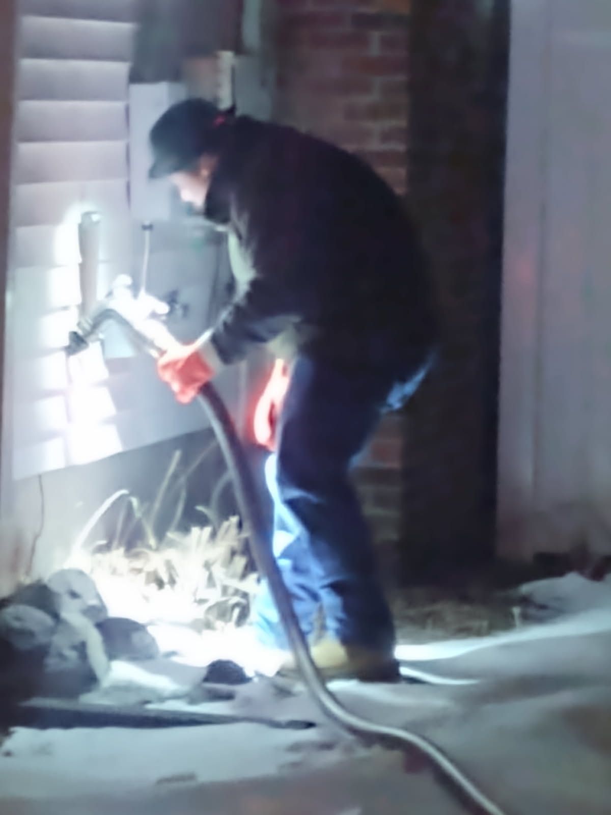 Person using a power tool beside a brick wall at night, with a bright work light and cables on the ground