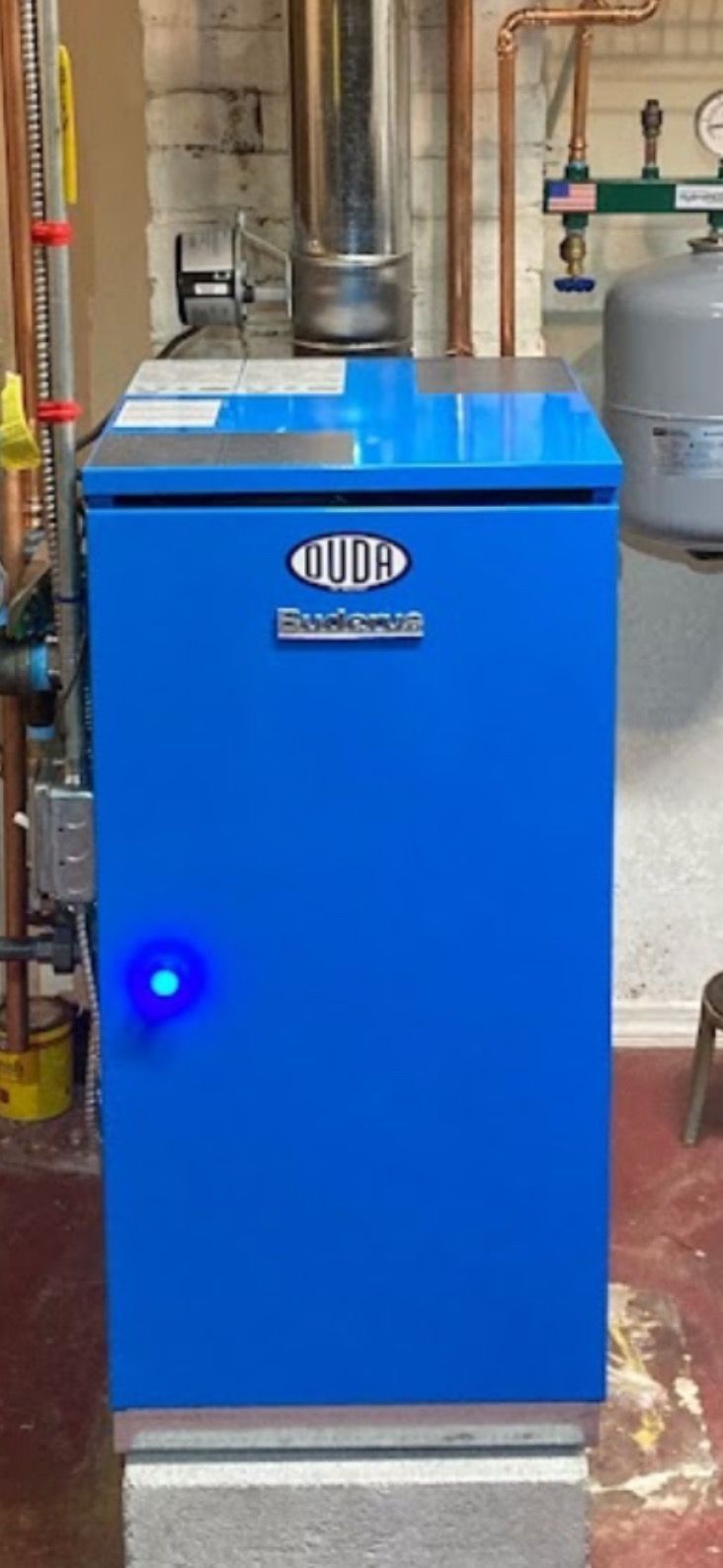 Blue industrial boiler or furnace in a basement with visible pipes and ducting