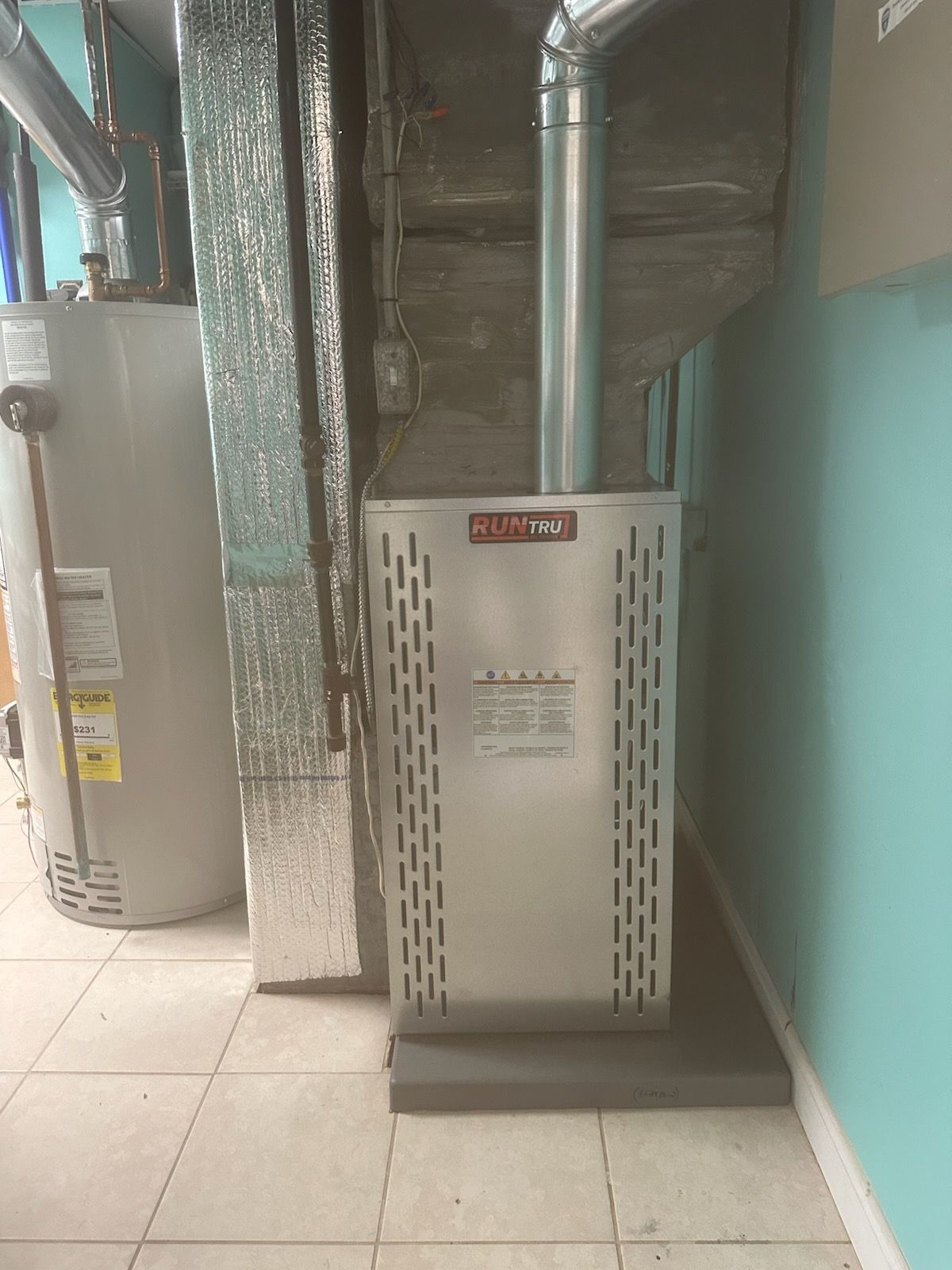 Boiler room with metal HVAC units, pipes, and a tiled floor beside a teal wall.