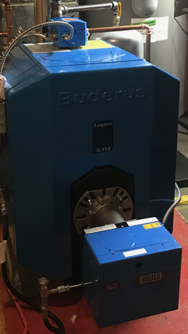Two large outdoor AC units mounted on a wall, with a yellow bucket on the wet floor below.