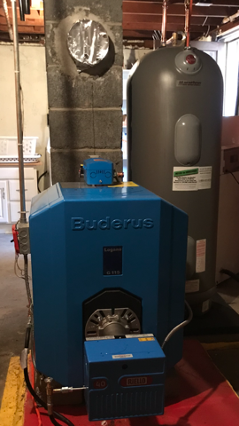 Blue Buderus boiler beside a tall gray water heater in a basement utility room.