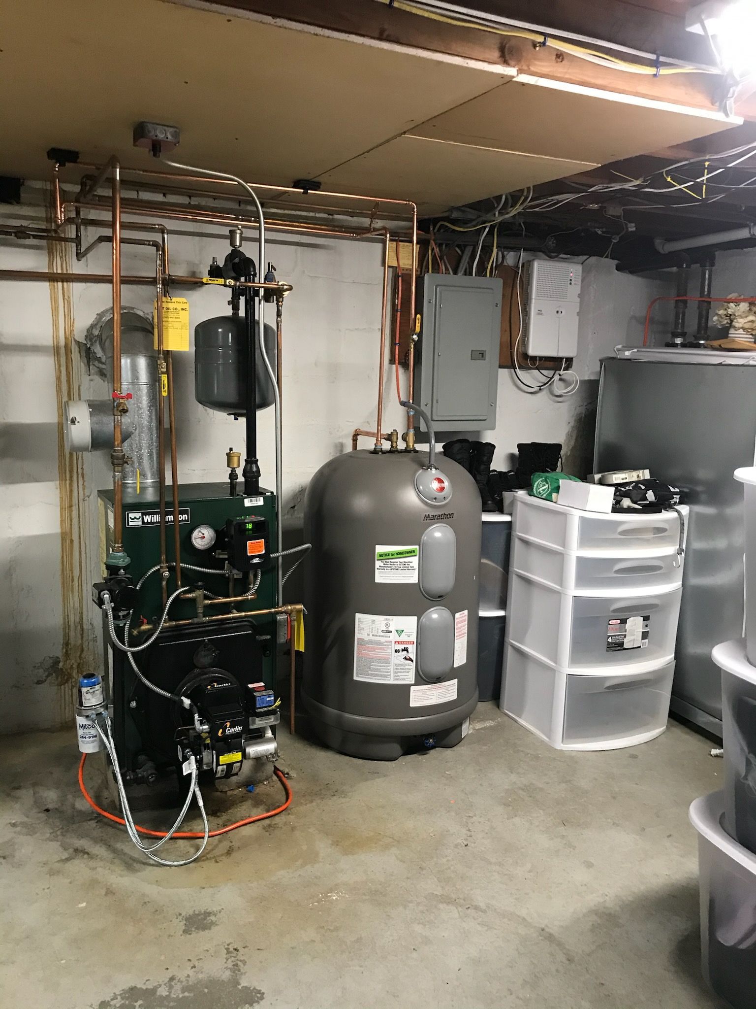 Basement utility room with boiler, water heater, pipes, and storage drawers.