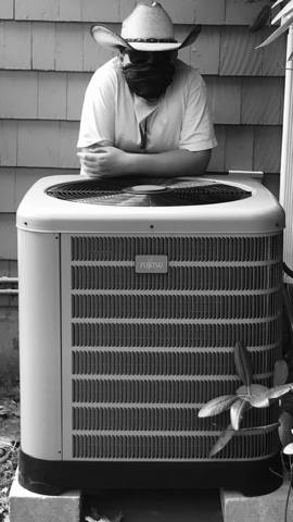 Worker in a hard hat leaning on a rooftop HVAC unit outdoors