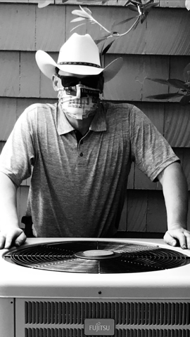 Person wearing a skull mask and cowboy hat stands behind a grill, holding the sides.