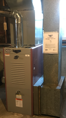 Basement furnace and ductwork beside a metal support column with an inspection tag.