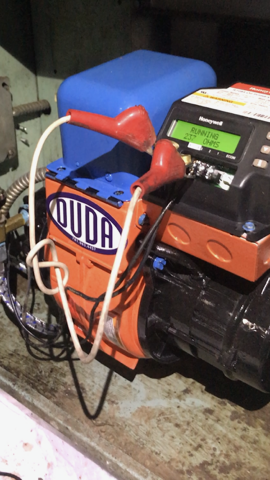 Blue-and-orange portable generator with red handles on a concrete floor, next to a wall outlet.
