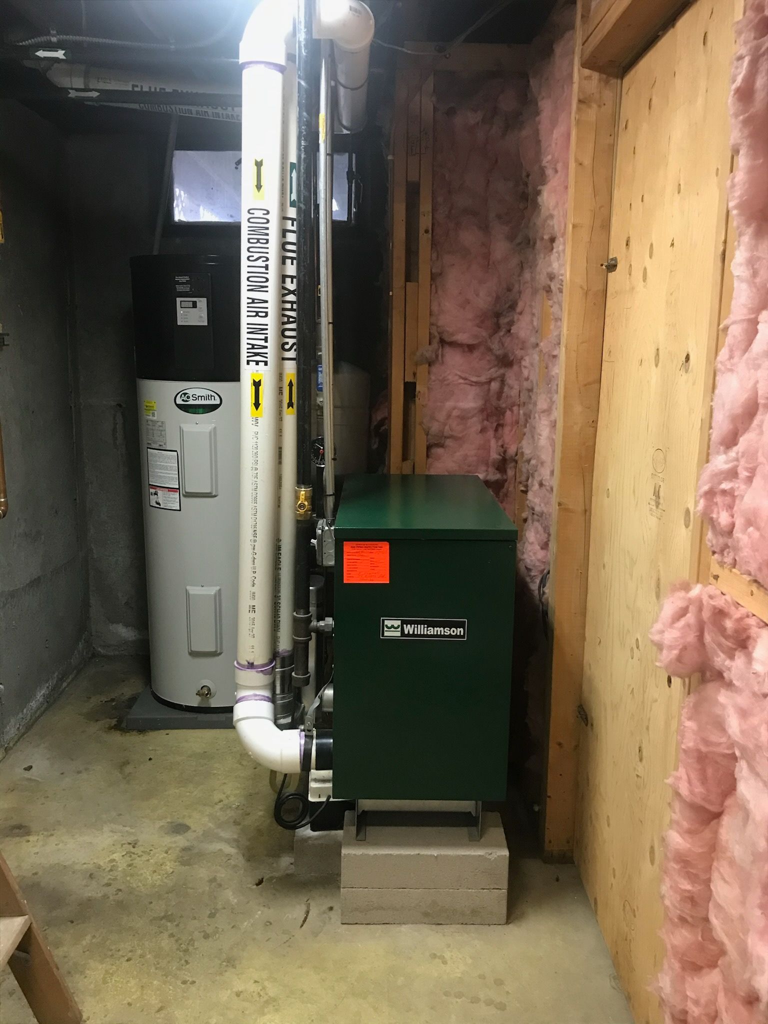 Basement utility room with furnace, water heater, and exposed pink insulation along the walls.