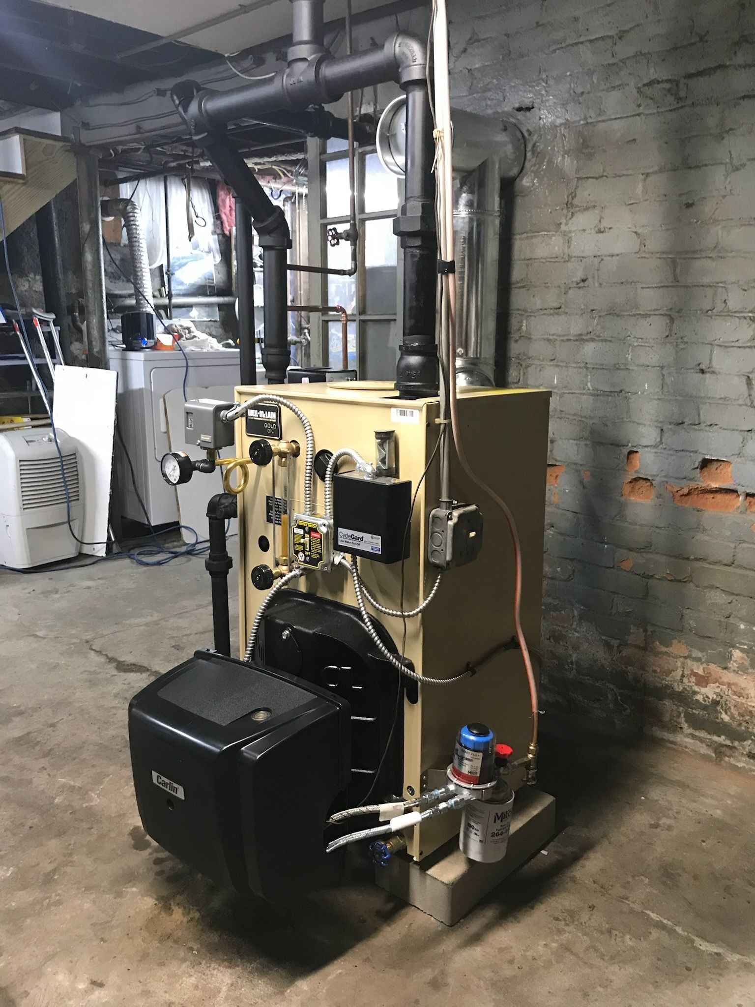 Yellow boiler in a basement with pipes and gauges against a concrete wall.