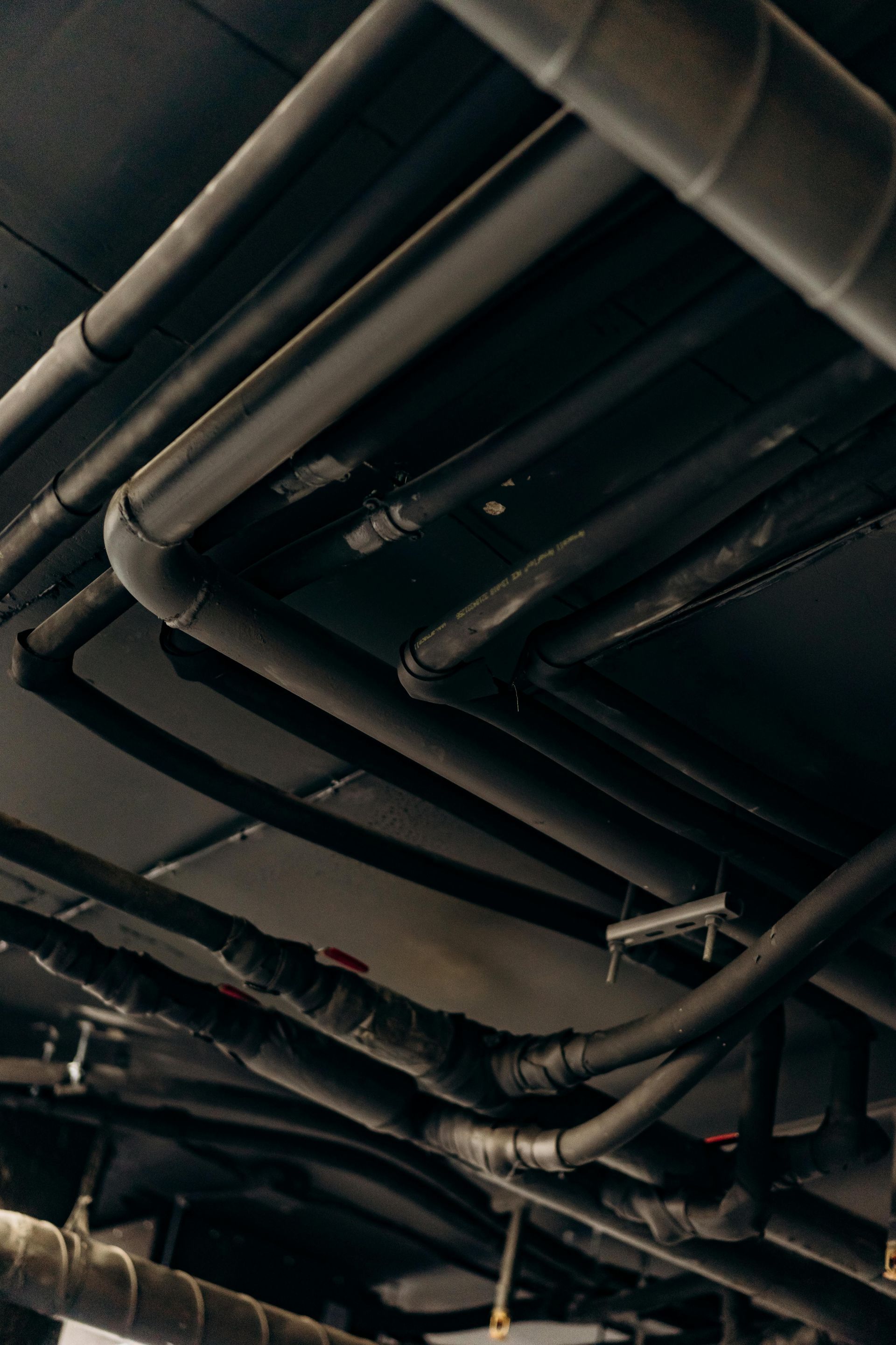 A low-angle view of several black industrial pipes running across a dark ceiling.