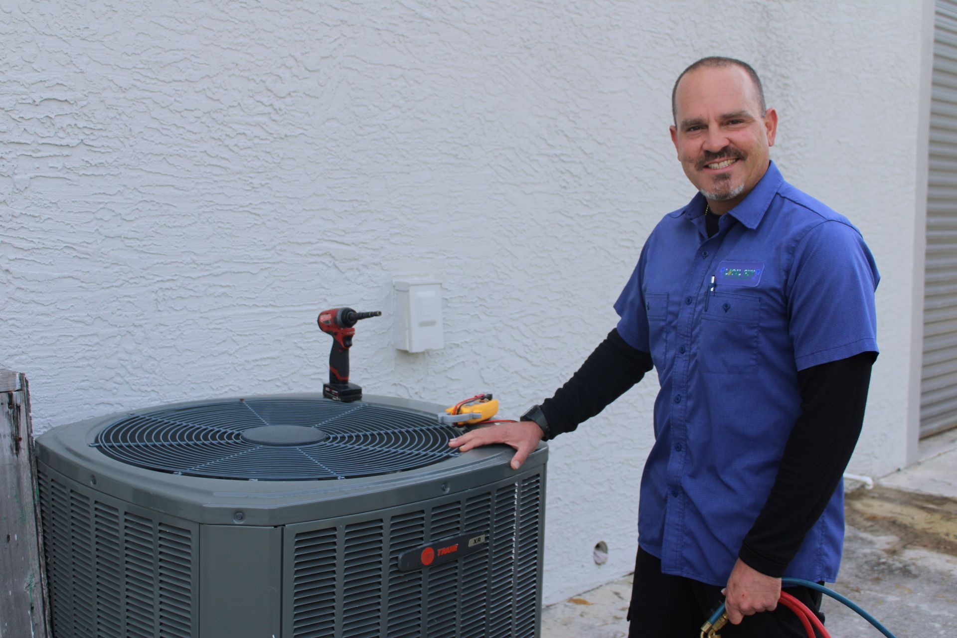A Local Guy technician in a blue shirt is standing next to an air conditioner.