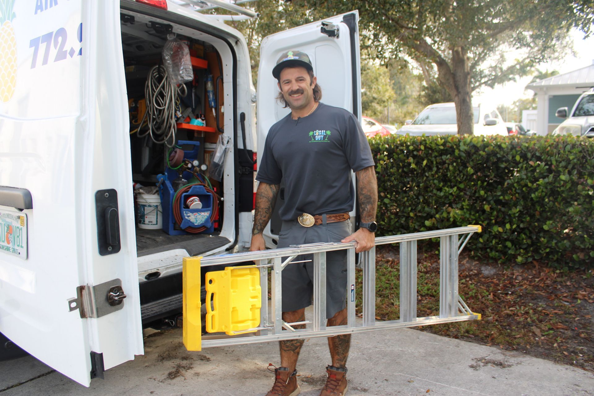 A Local Guy technician is holding a ladder in front of a van.