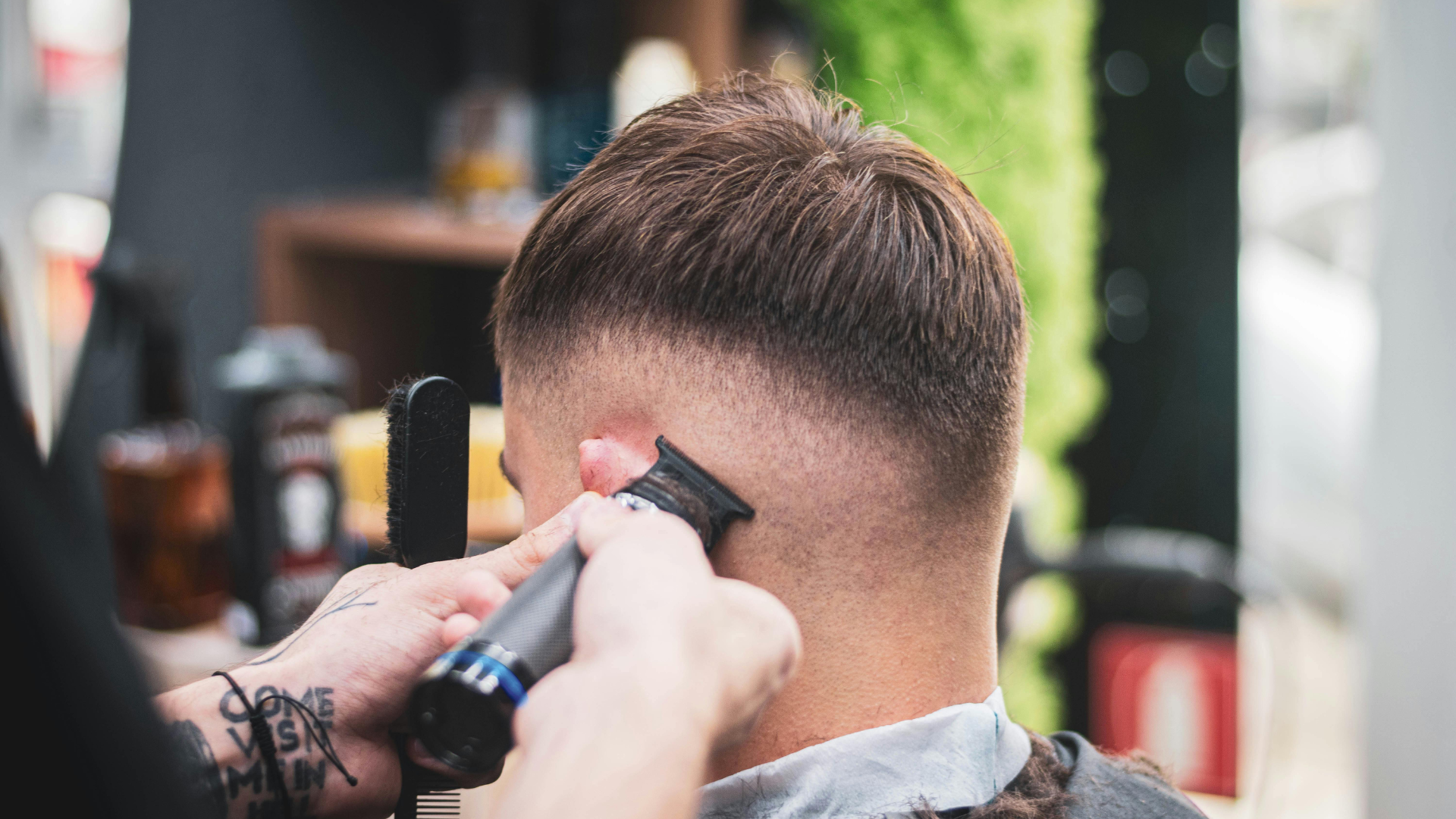 A barber uses electric clippers to fade the hair on the side of a person's head in a salon setting.