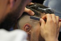A barber uses a straight razor to carefully edge and shave the hair around a client’s ear.